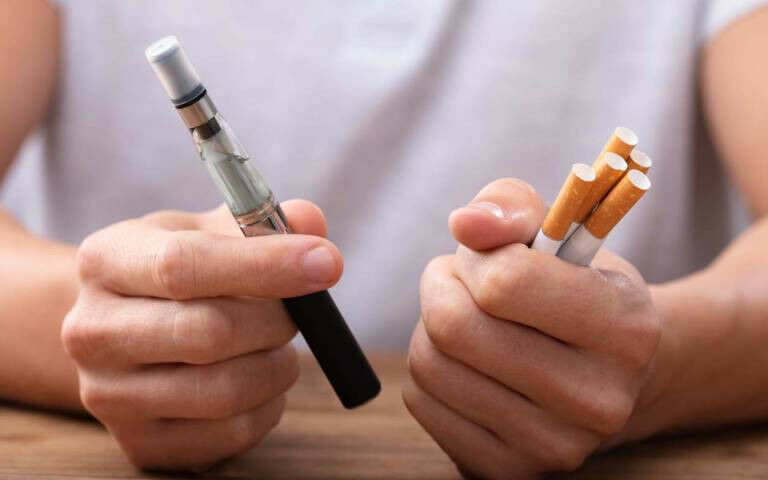 young person holding cigarettes and an e-cigarette