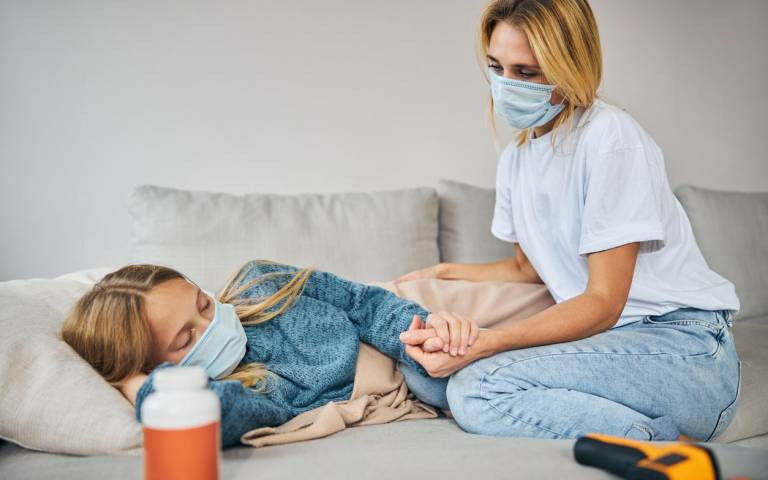 An older woman holding hands with a sick girl lying on the sofa