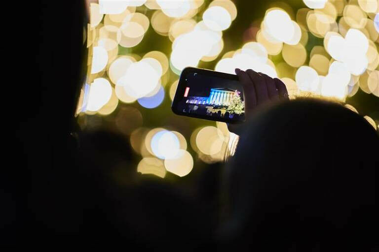 A person holds up a smartphone capturing a photo of a brightly lit building in f