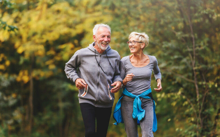 older couple jogging in the park and smiling