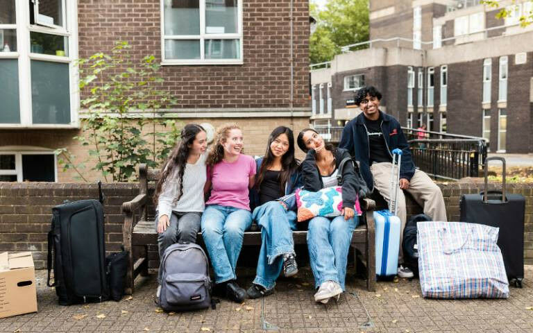 A group of students sitting on a bench at UCL Accommodation with various pieces