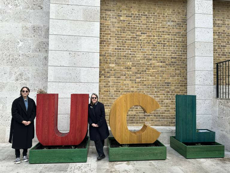 Two people stand beside large, colourful letters spelling ’UCL’ outs