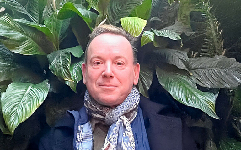 Sir Geoff Mulgan facing the camera with green plants behind him