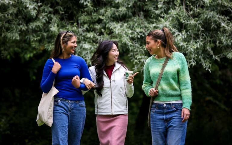 Three students walk towards the camera against a background of trees and greener