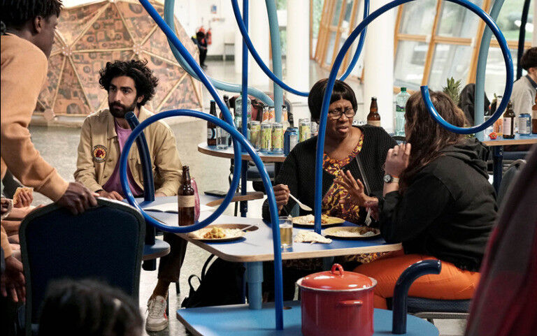 Four people sitting, talking and eating at a table, next to art and sculptures